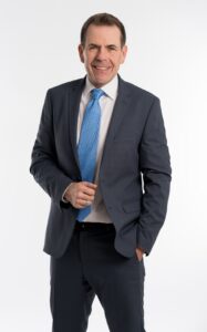 Porträt von Harald Vilimsky: Kurze Haare, mittelblaue Krawatte und dunkelblauer Anzug, weißes Hemd. Er lächelt lebhaft.