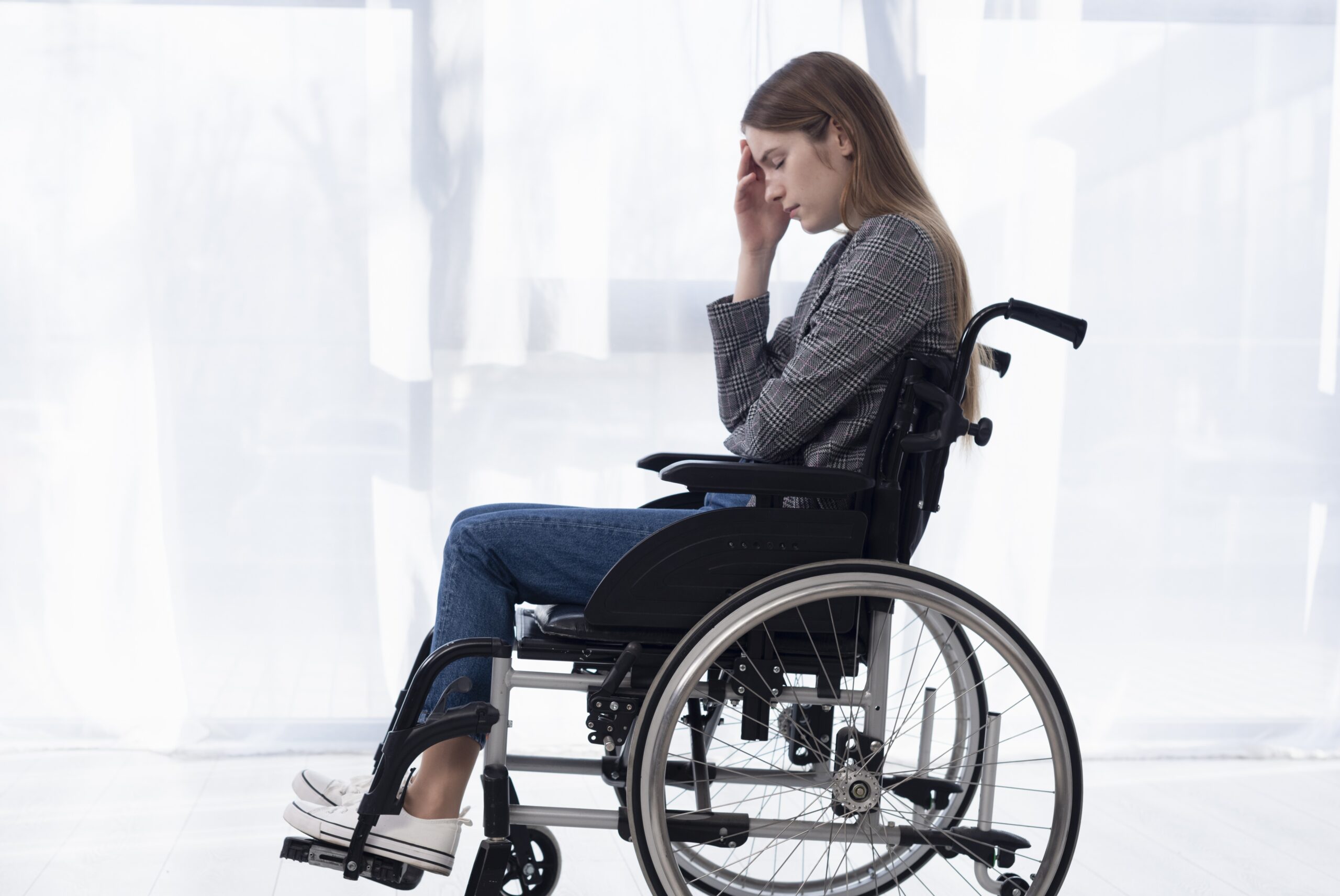 Eine junge Frau im Rollstuhl greift sich verzweifelt an den Kopf