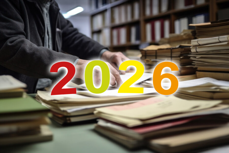 Ein älterer Mann arbeitet an einem Berg von Unterlagen, im Vordergrund ist der Schriftzug "2026"